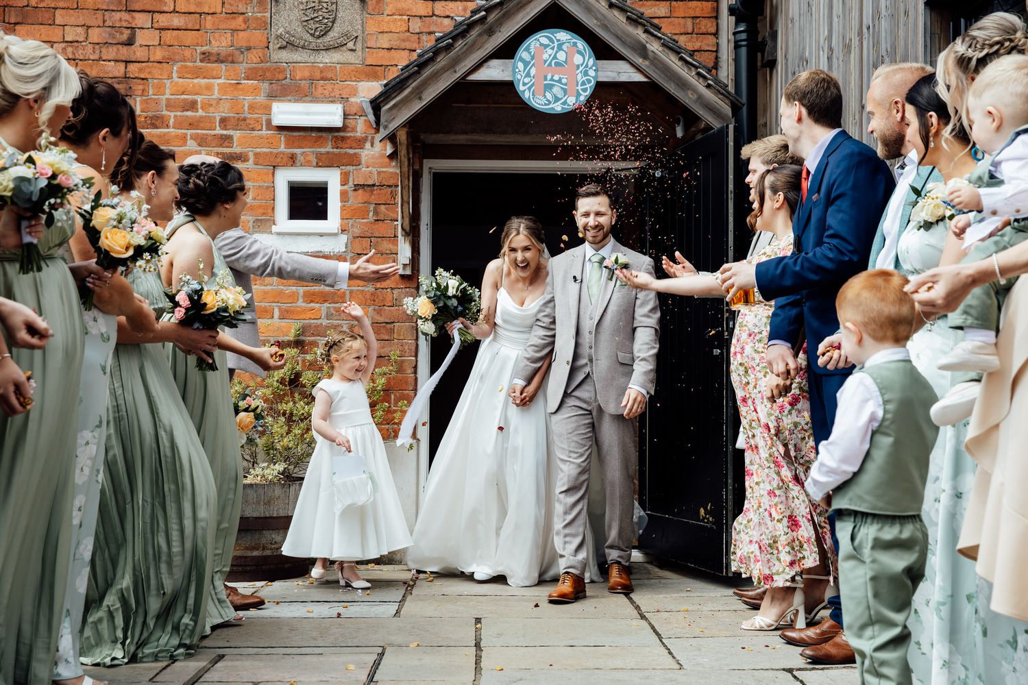 Wedding ceremony processional with bridesmaids in sage green dresses outside brick church.