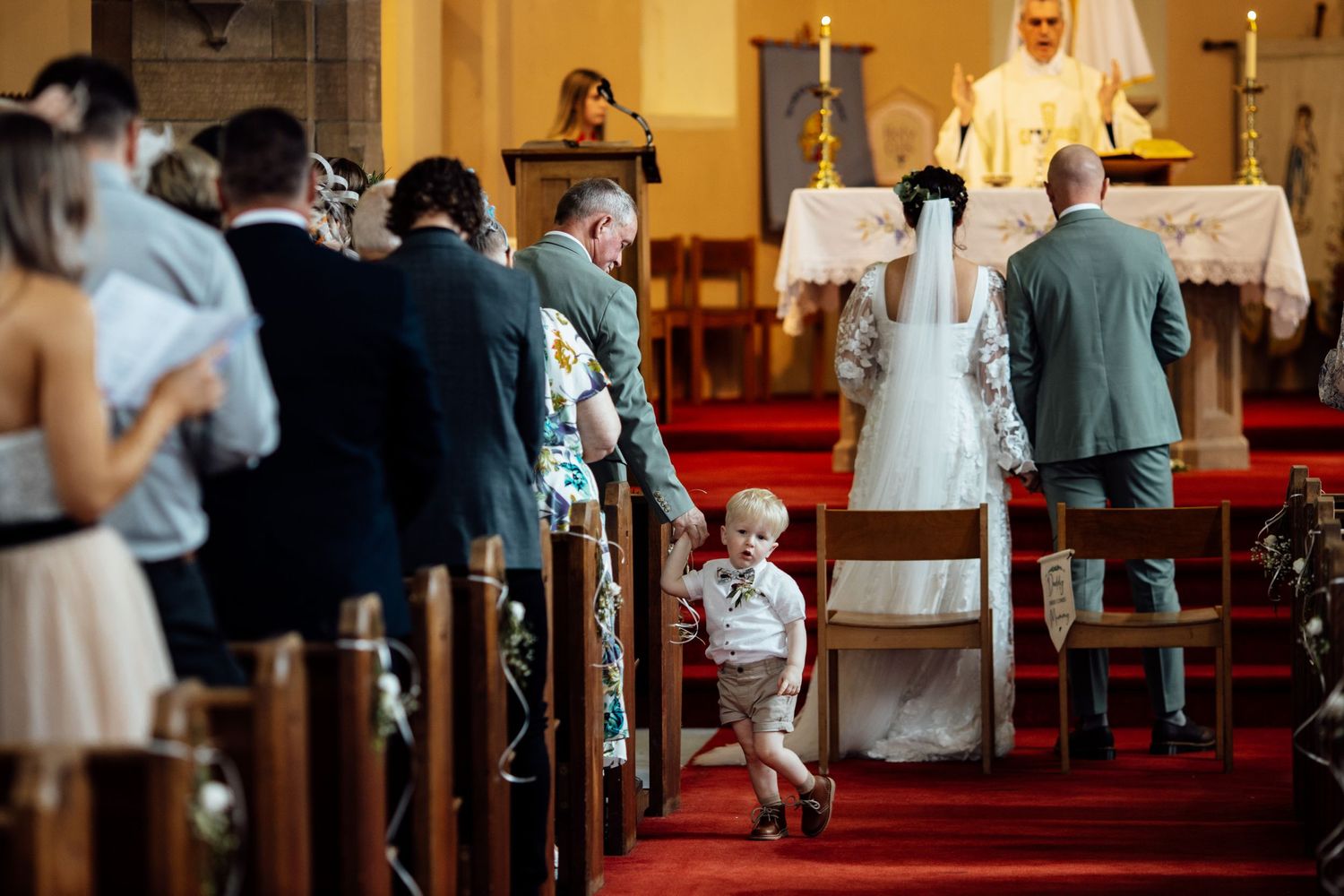 Interior of a church with wooden pews and red carpet during a wedding ceremony.