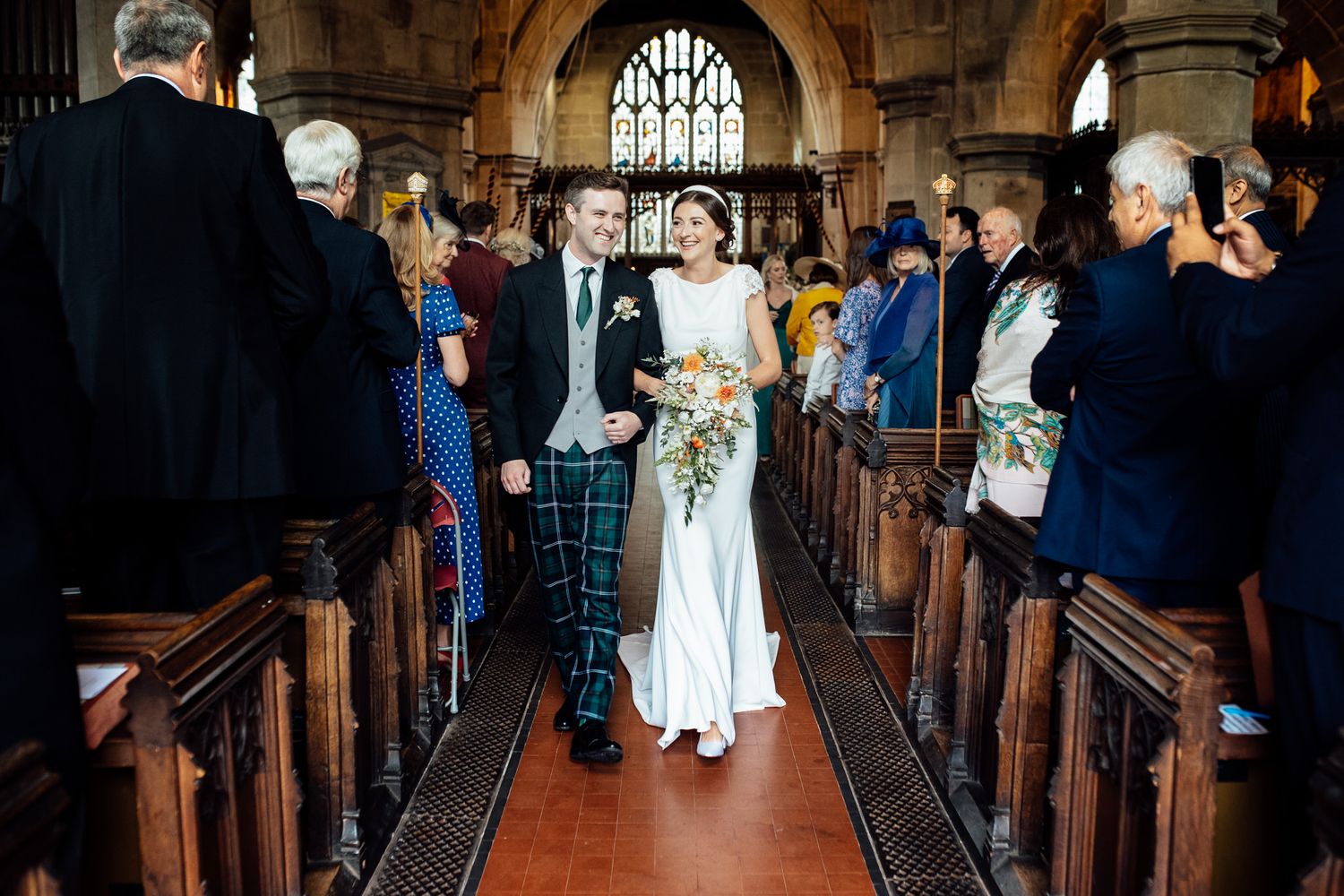 Wedding ceremony procession in a grand church aisle with wooden pews.