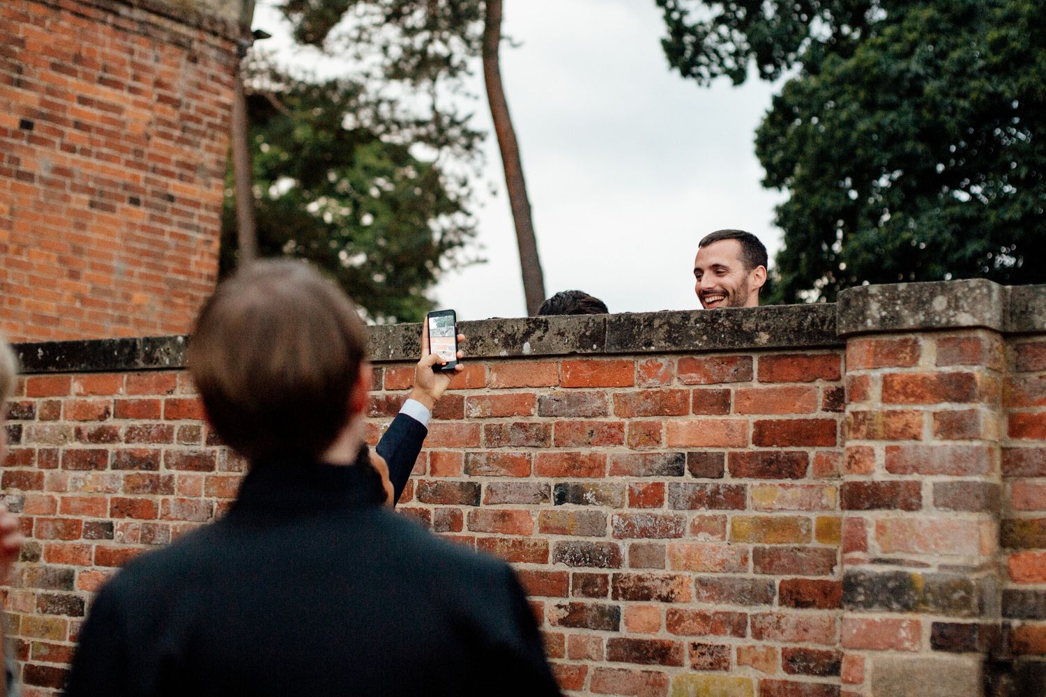 Person looking over brick wall while being photographed from behind.