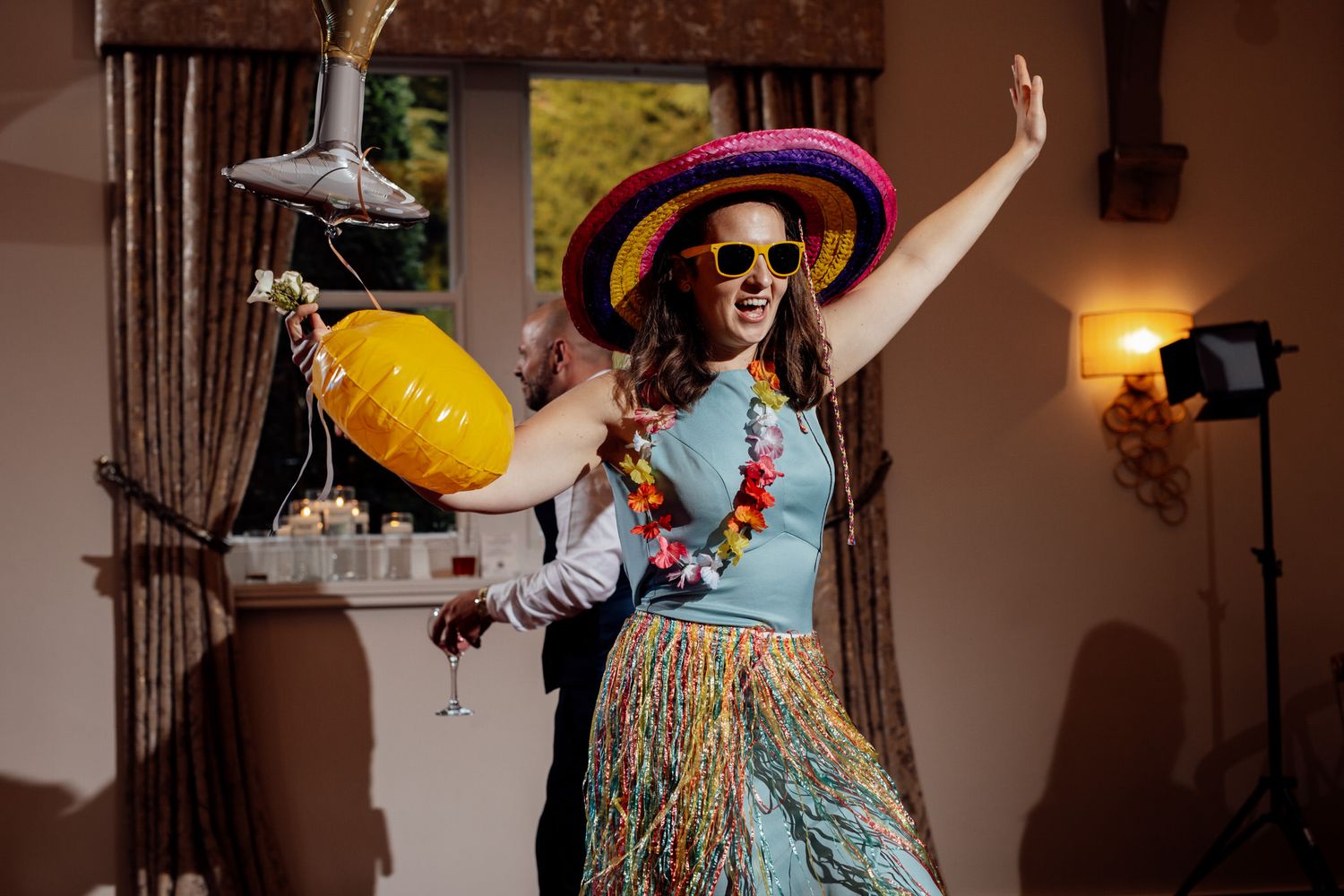 Wedding guest in colorful attire and sun hat dances with party props.