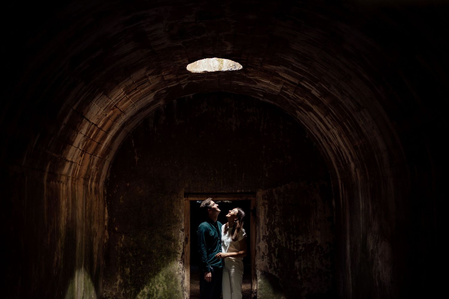 A silhouetted couple stands in a dramatic stone tunnel or archway.