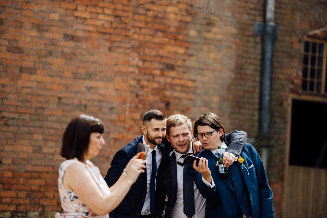Group of wedding guests chatting and laughing outside a historic brick building.