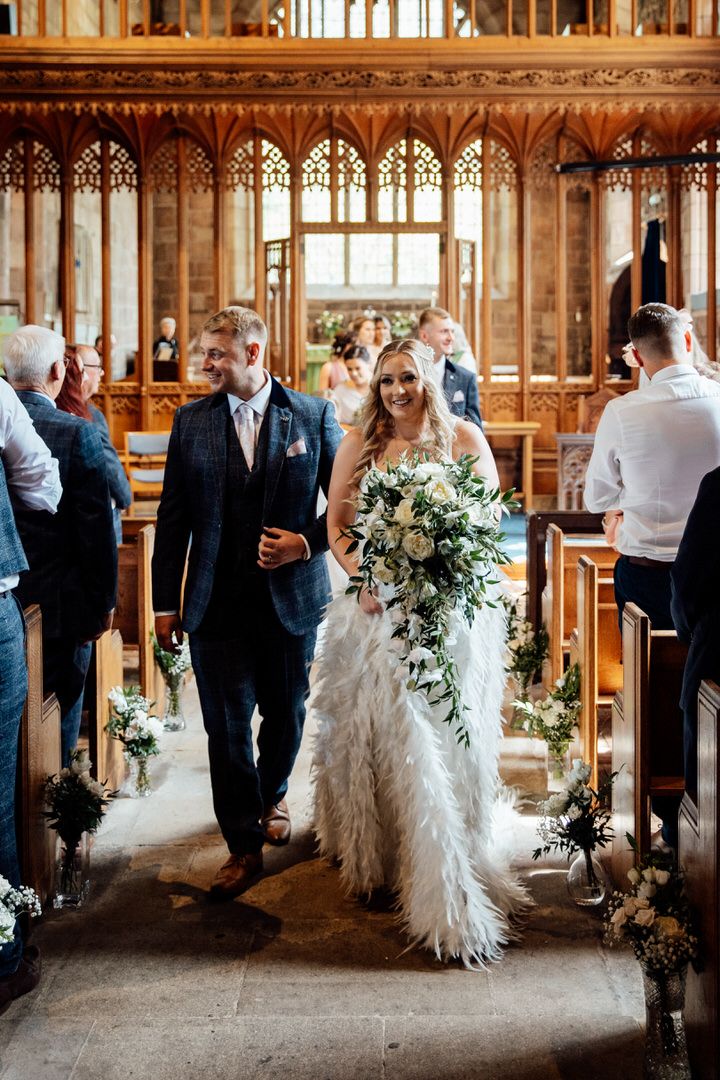 Wedding party processes through an ornate wooden church interior with floral arrangements.