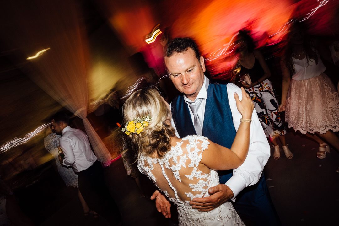 Couple dancing energetically at a wedding reception with motion blur and colorful lighting effects.