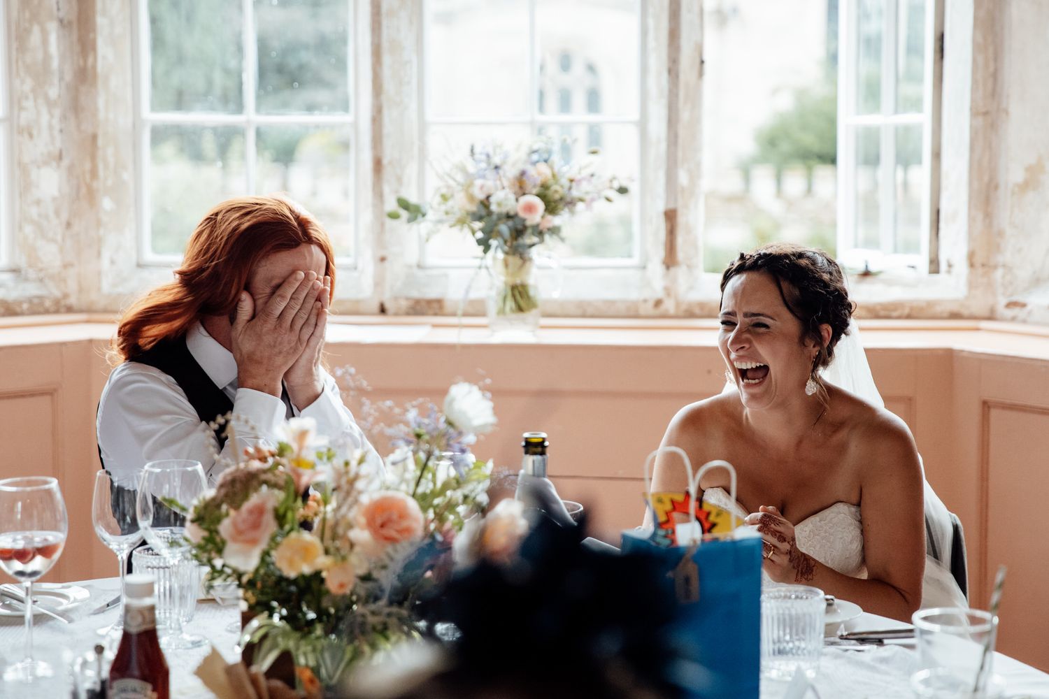 Candid moment of laughter shared at wedding reception with floral centerpiece.