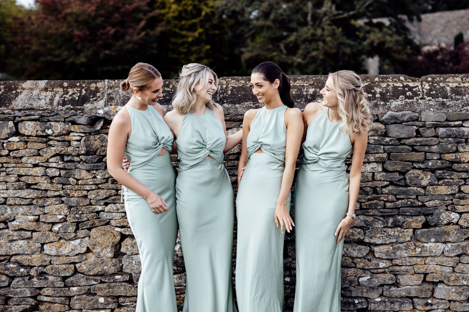 Bridesmaids in light blue dresses posing against a rustic stone wall.