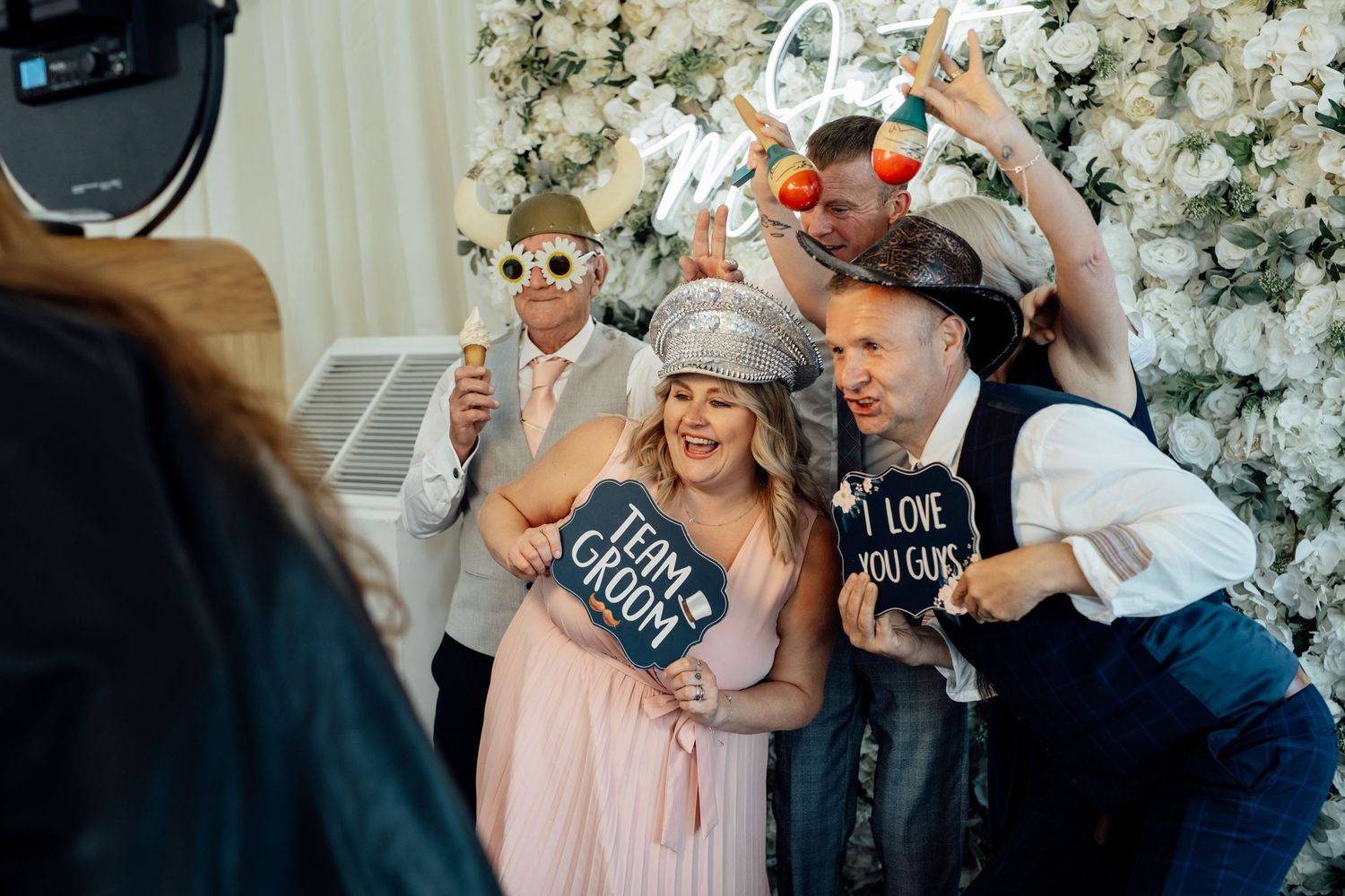 Wedding party celebrates joyfully with champagne under white floral decorations at an elegant reception.