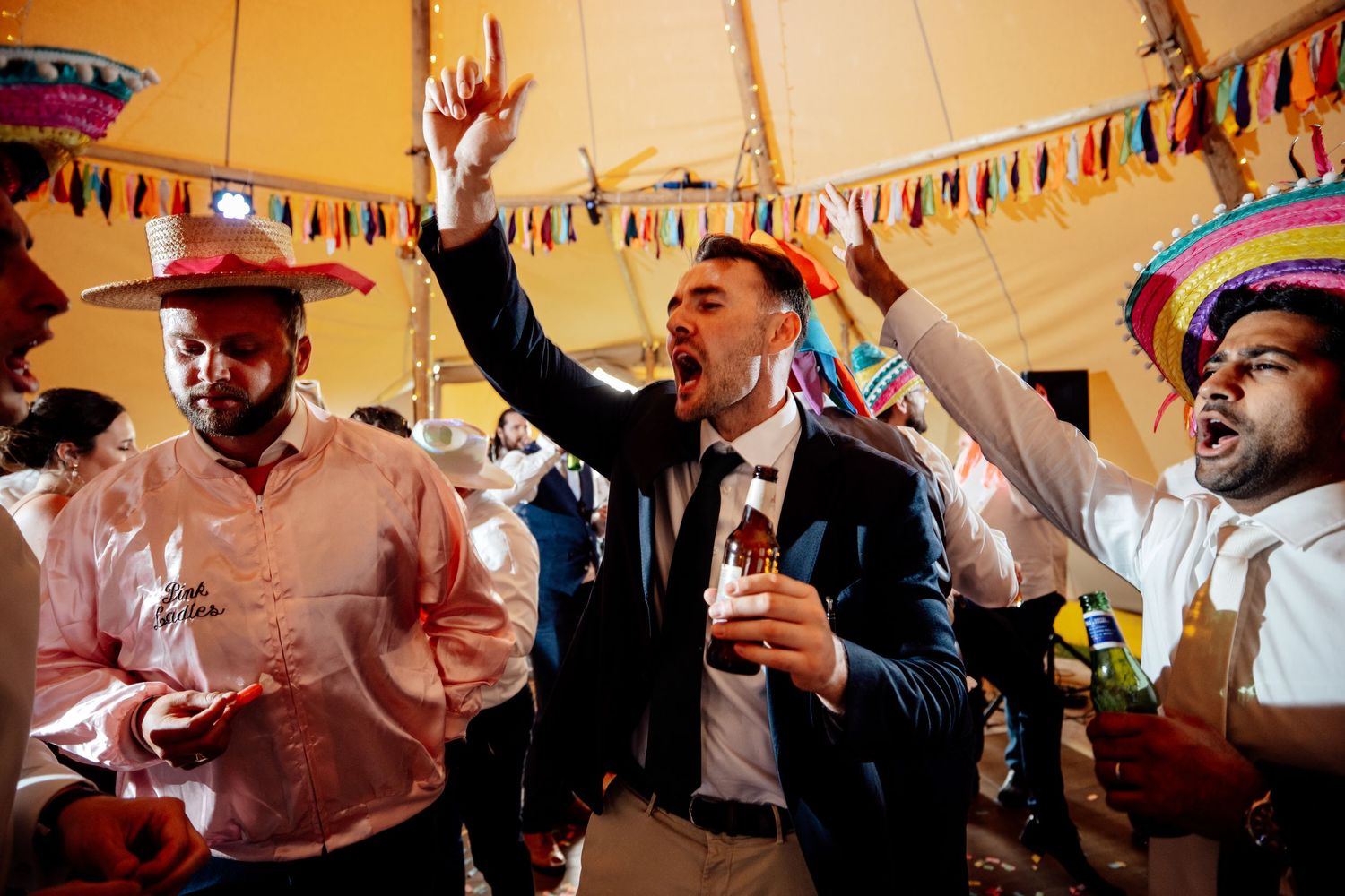 Wedding celebration under a tent with colorful bunting decorations and dancing guests.