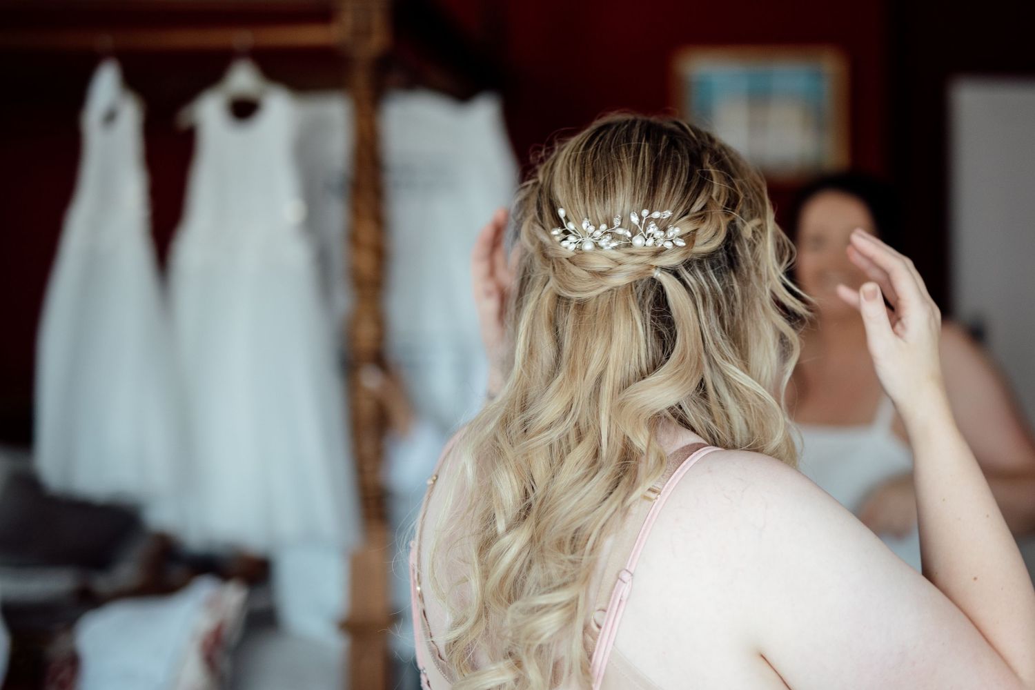 Elegant bridal hairstyle with delicate crystal hairpiece shown from behind with wedding dresses hanging.