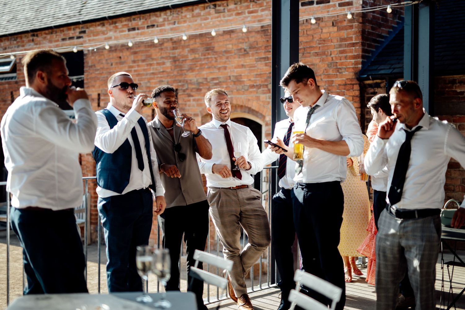Wedding guests mingling and socializing outside brick venue during daytime celebration.