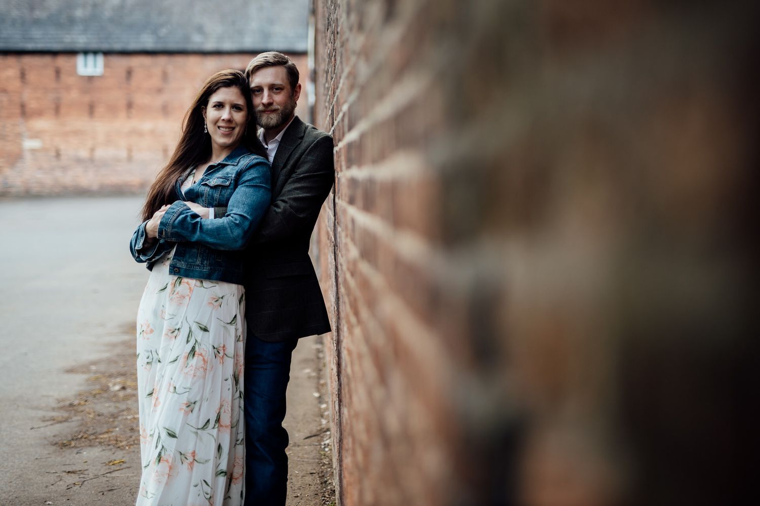 A couple embraces against a rustic brick wall in an outdoor setting.