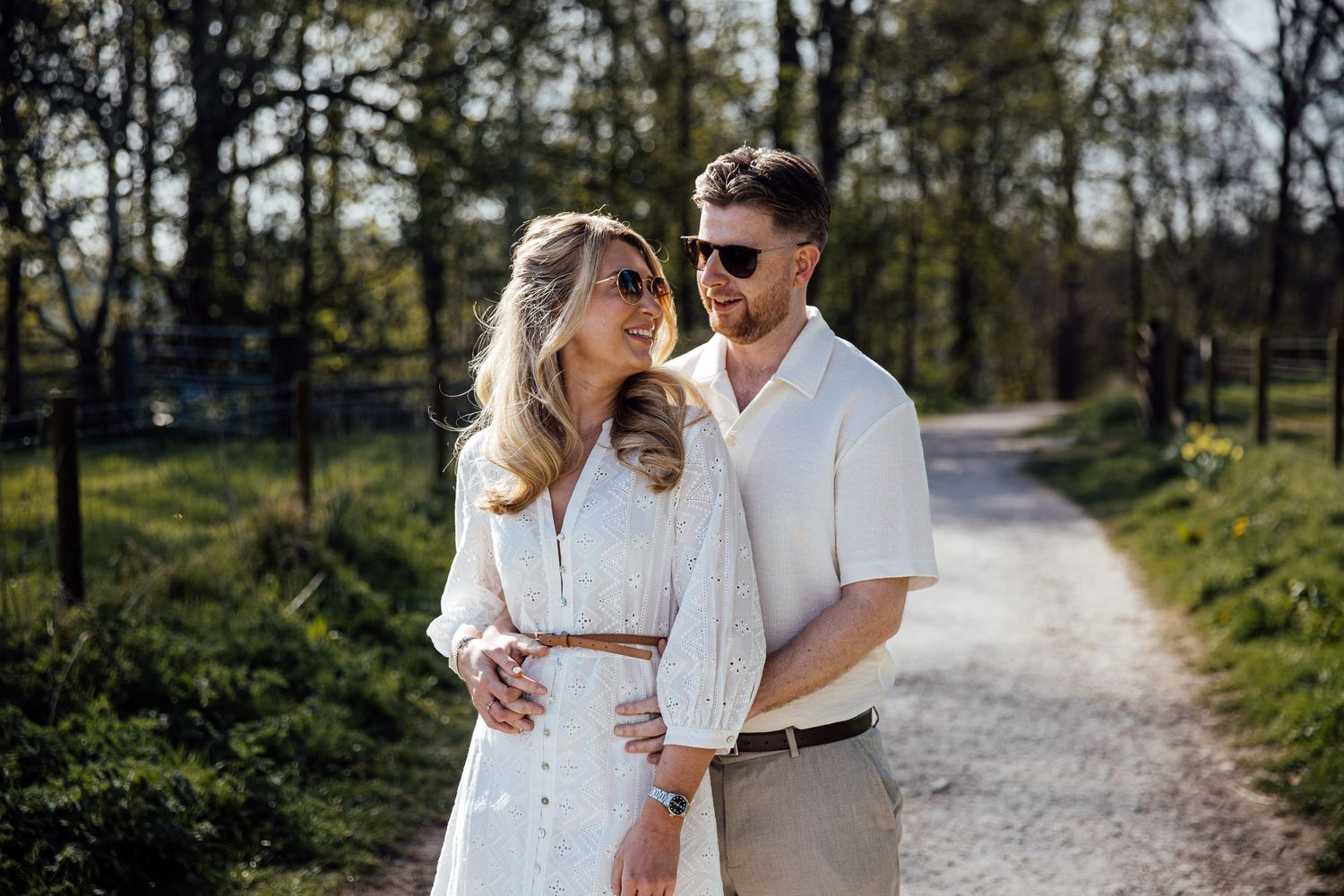 A romantic couple walking together on a tree-lined path during an outdoor photo session.
