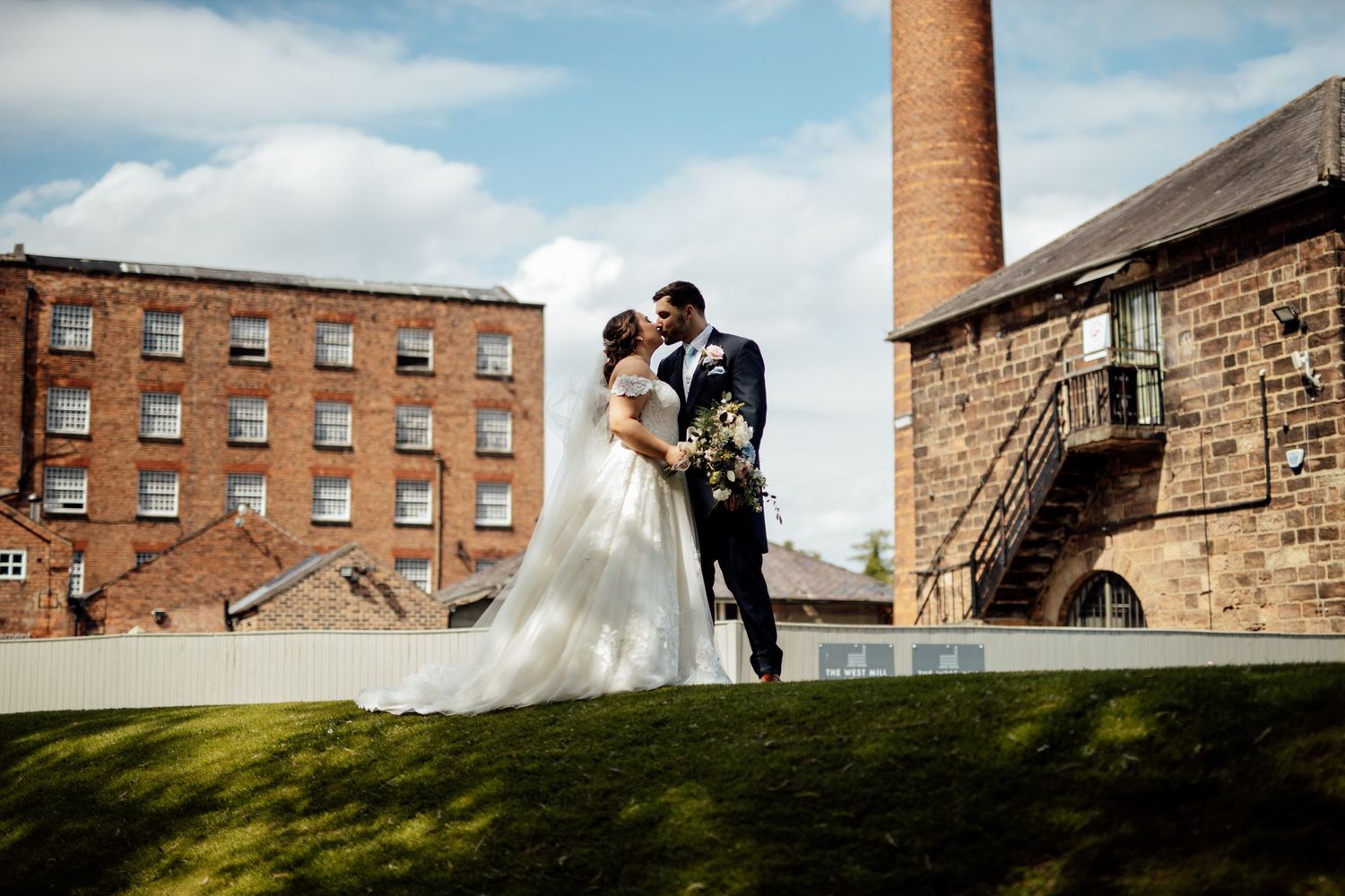 Wedding couple photographed against industrial brick buildings and chimney tower.