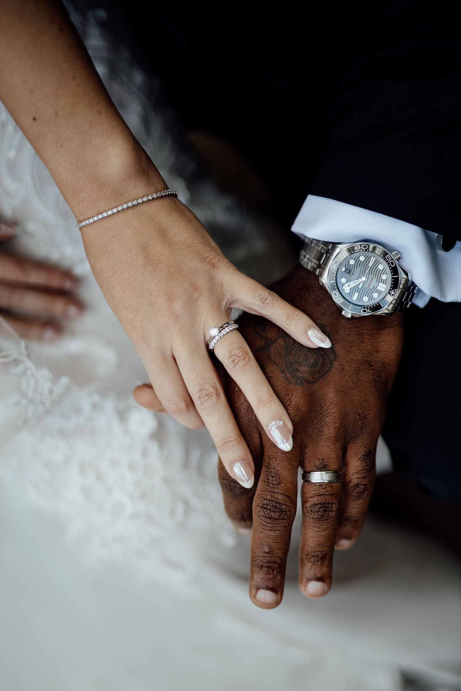 Close up of hands with wedding rings and jewelry against white fabric.