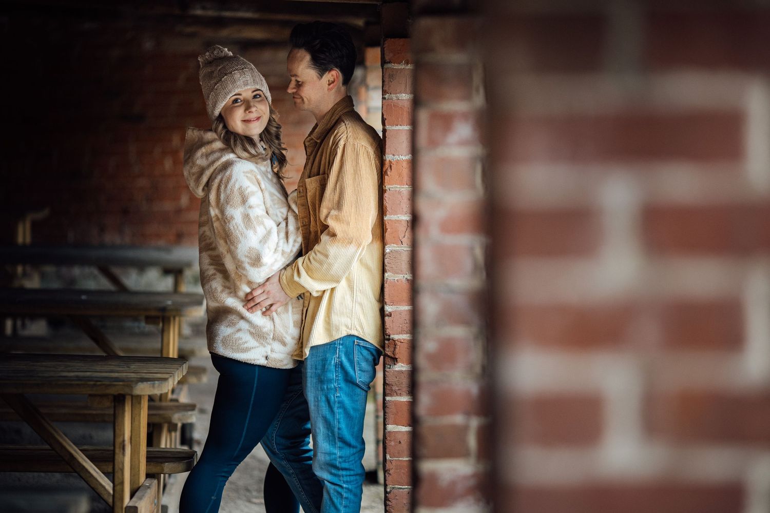 Intimate couple's portrait against a brick wall background during a winter photoshoot.