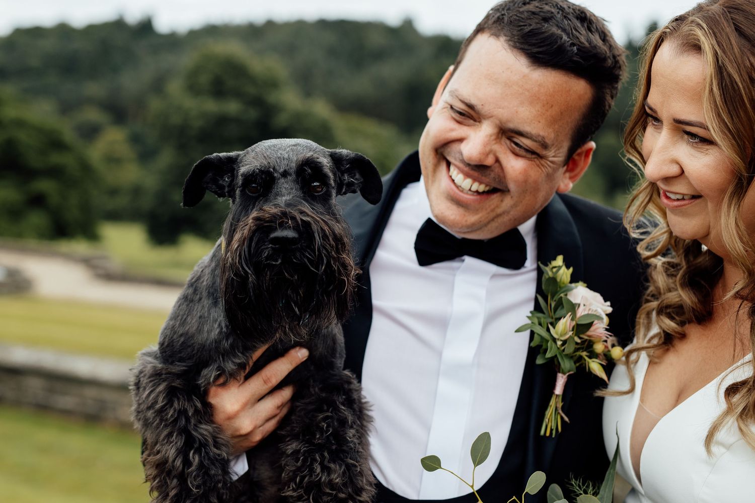 Wedding couple posing with their black dog outdoors.