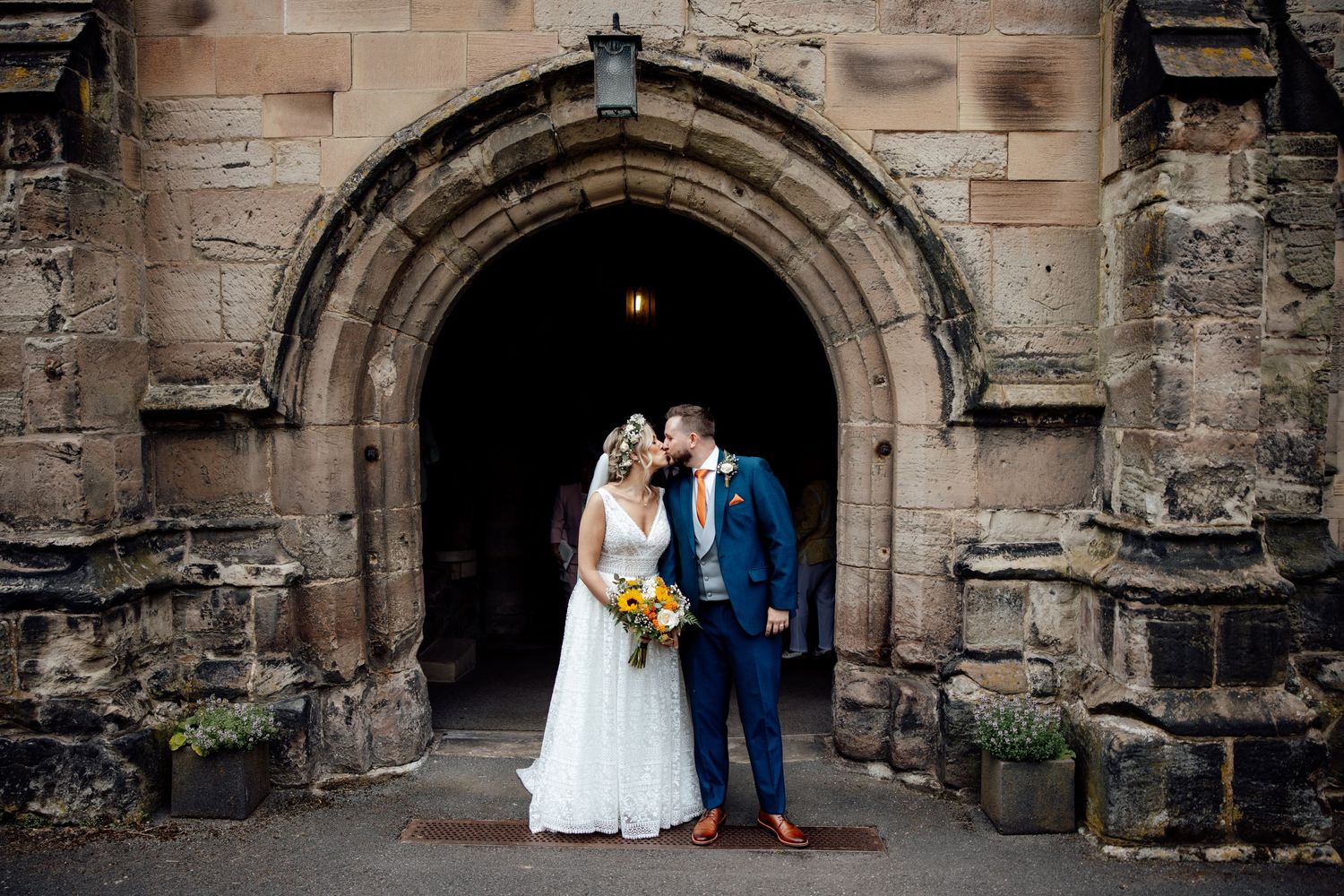 A wedding couple poses under a historic stone archway entrance.