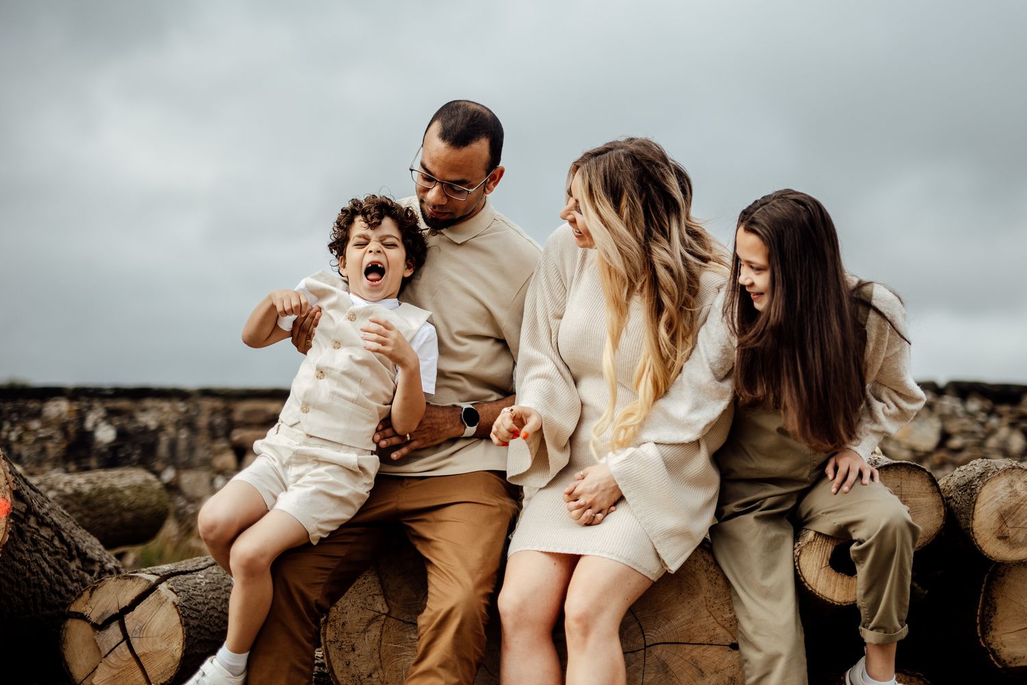 A family shares tender moments together while sitting outdoors in coordinated neutral outfits.