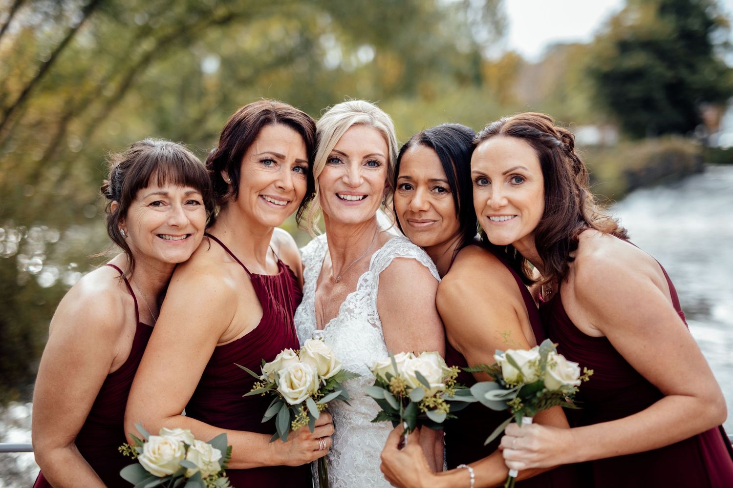 Bridesmaids in coordinated dresses holding white bouquets outdoors.