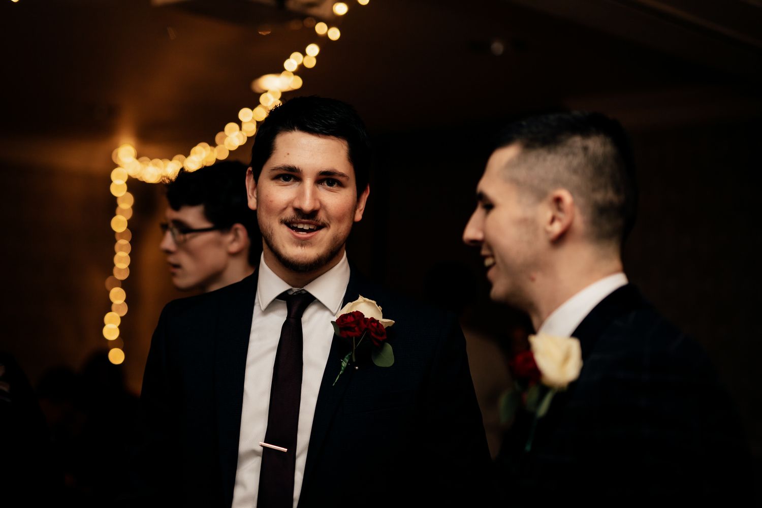 Wedding guests in formal attire gather at an elegant evening reception with warm lighting.