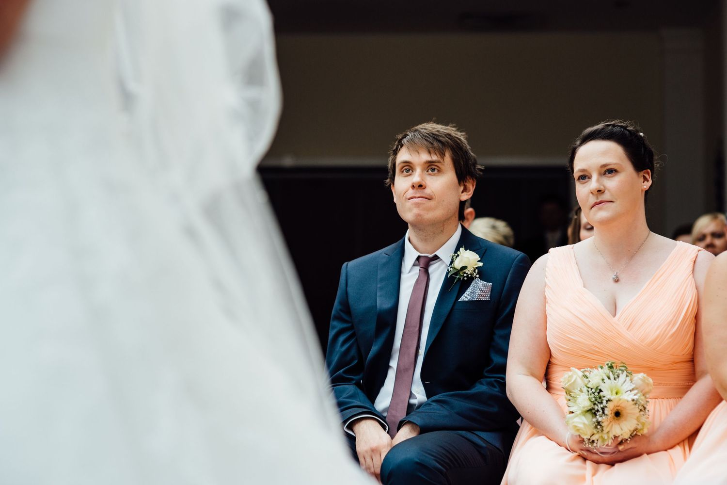 Wedding party members sit in a bright sunlit room during the ceremony.