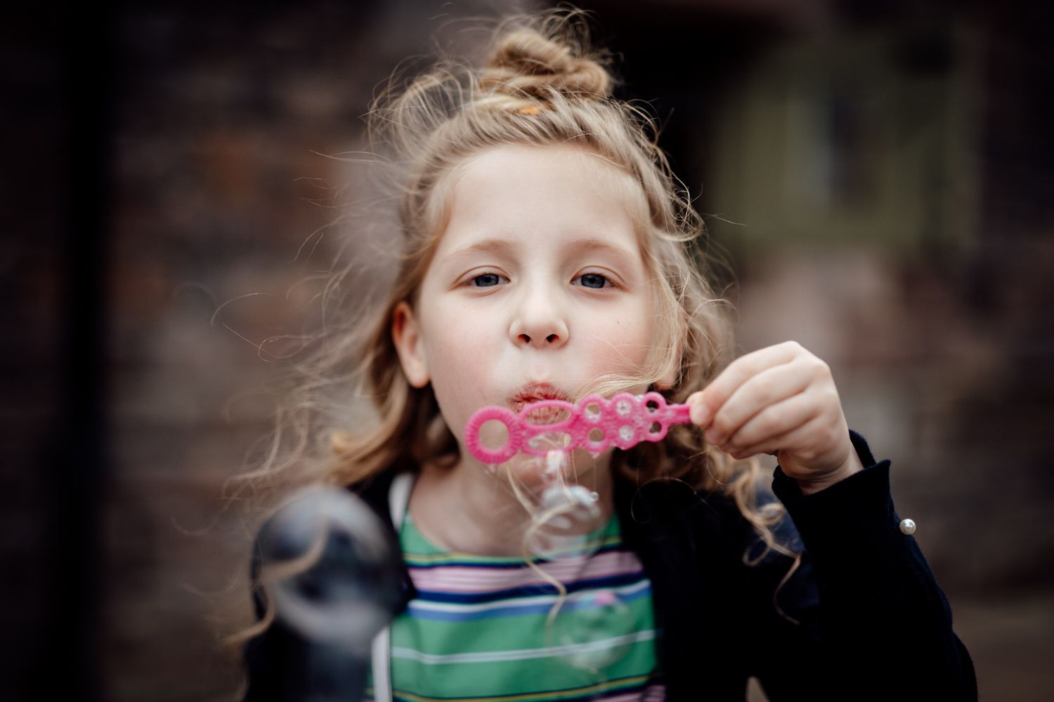 Young child blowing bubbles while wearing a green shirt in an outdoor setting.