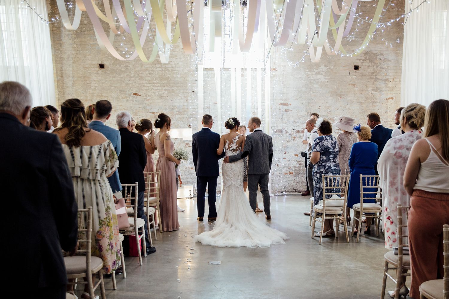 Elegant white wedding venue interior with guests seated at decorated tables.