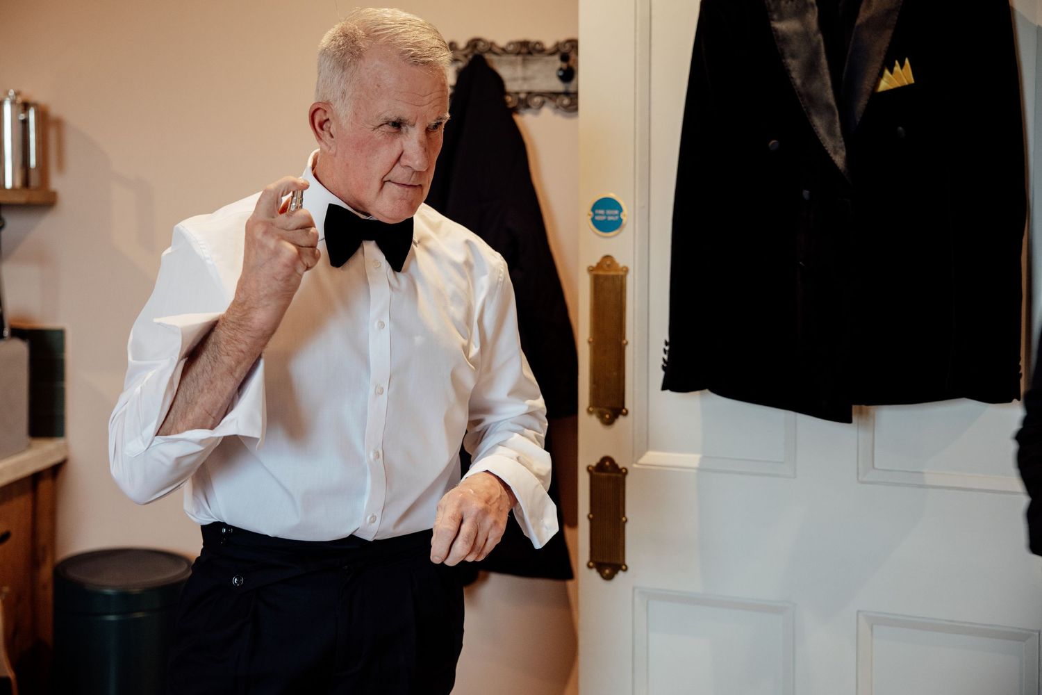 A person in a white dress shirt and bowtie adjusts their attire while getting ready.