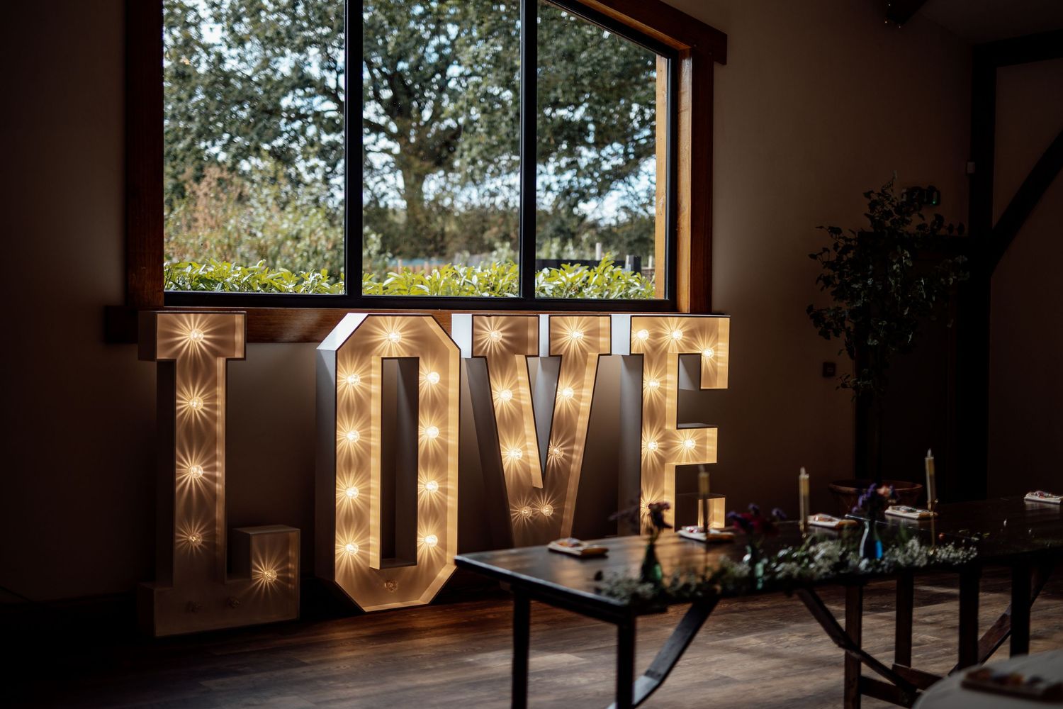 Illuminated LOVE marquee letters decorating a rustic wedding venue interior near a window.