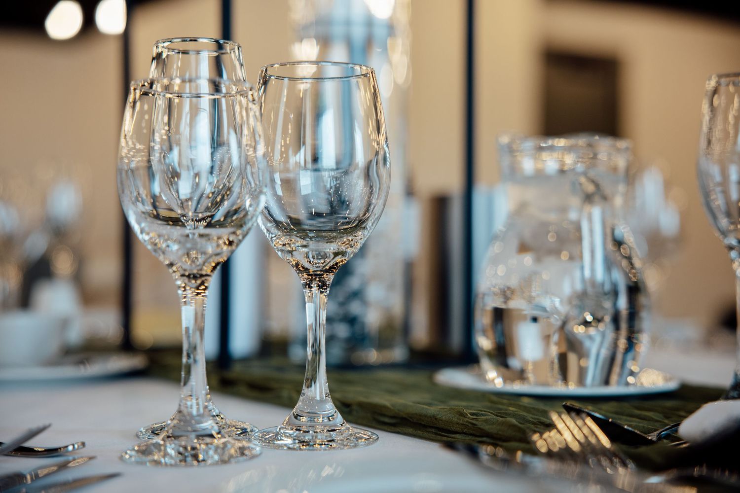 Two elegant crystal wine glasses on a white tablecloth at a formal dining table setting.