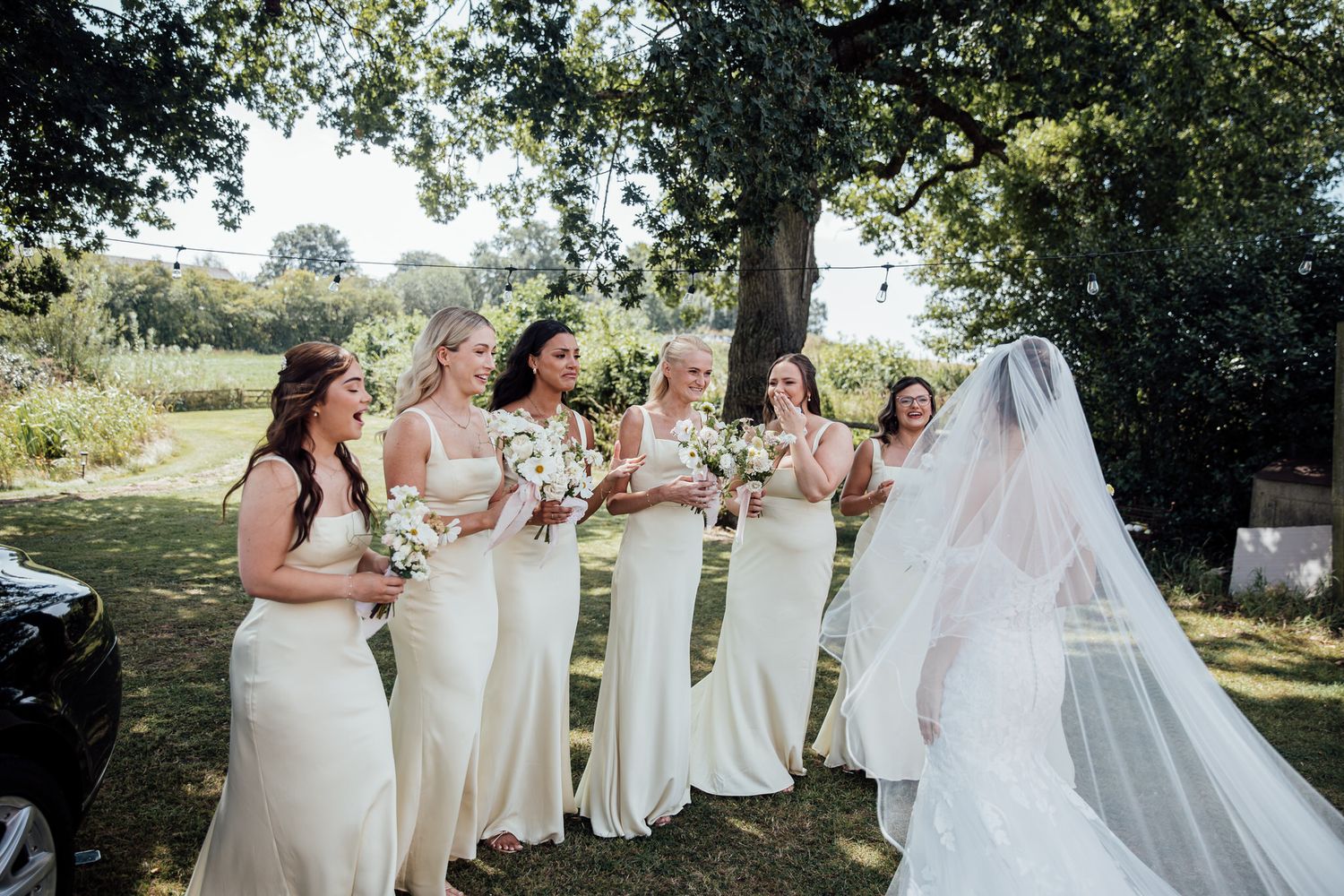 Bridesmaids in cream colored dresses pose together outdoors for wedding party photos.