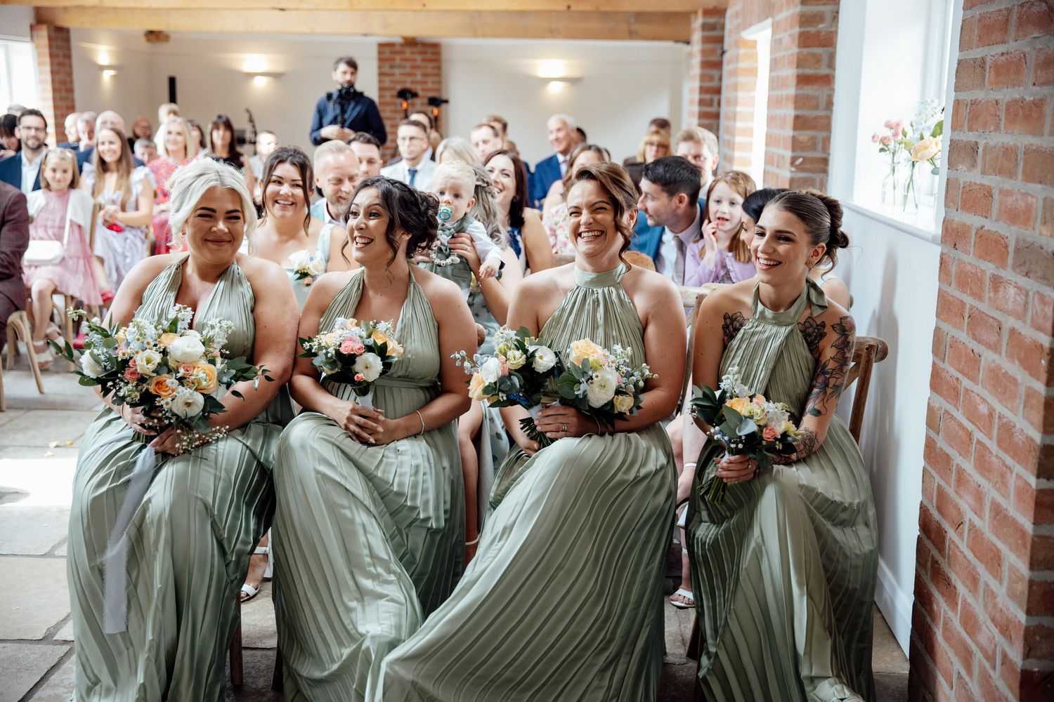 Bridesmaids in sage green dresses gather for photos in a bright indoor venue.