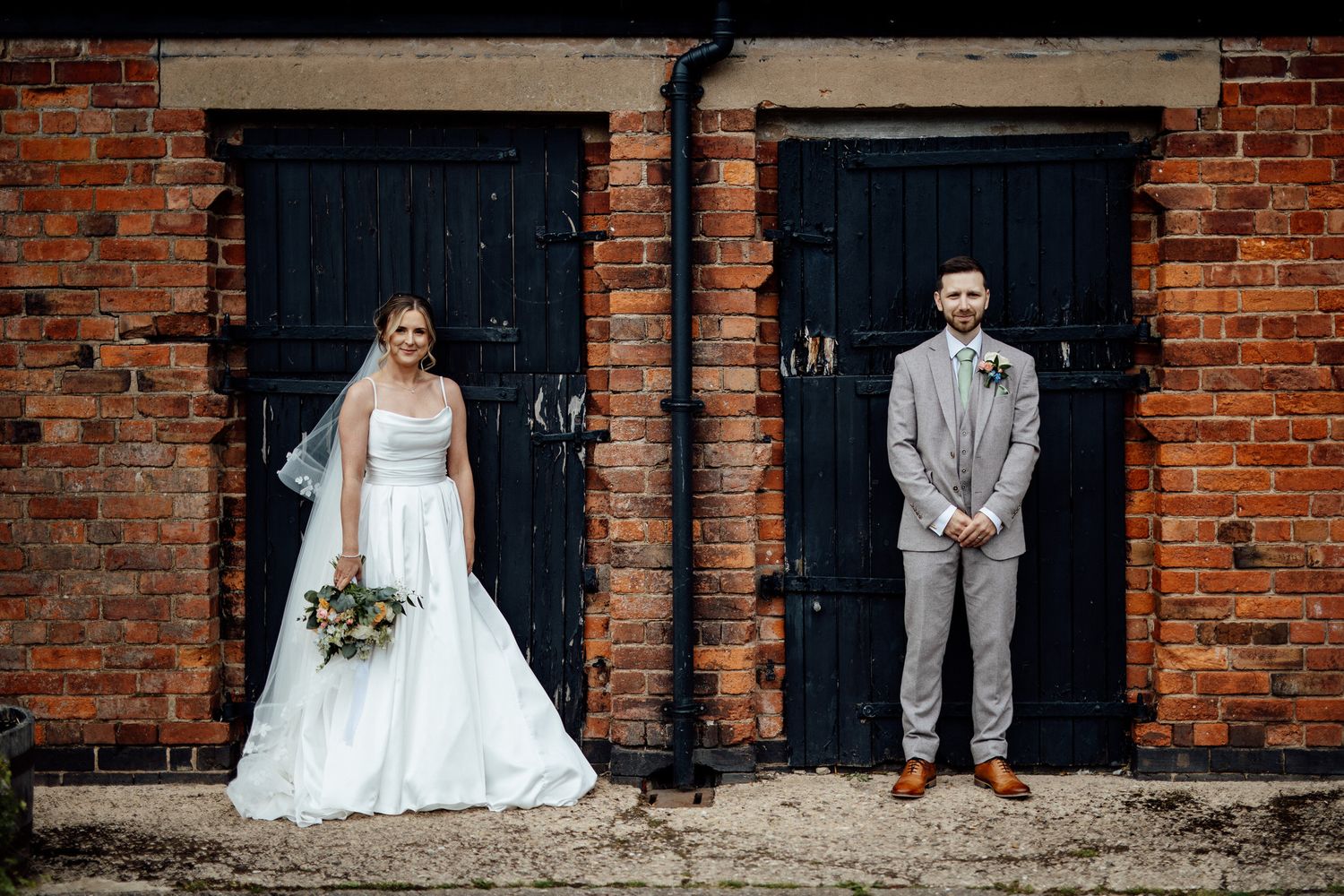 Wedding couple posing against rustic brick wall with black doors.