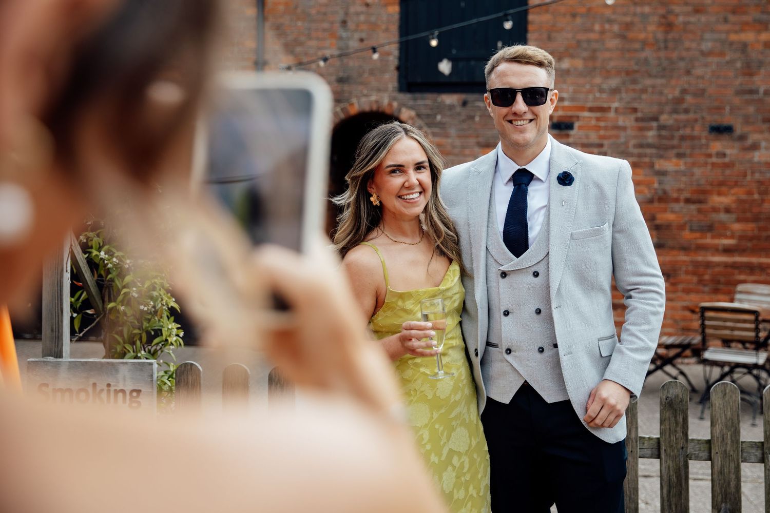 Wedding party members posing casually against brick wall backdrop.