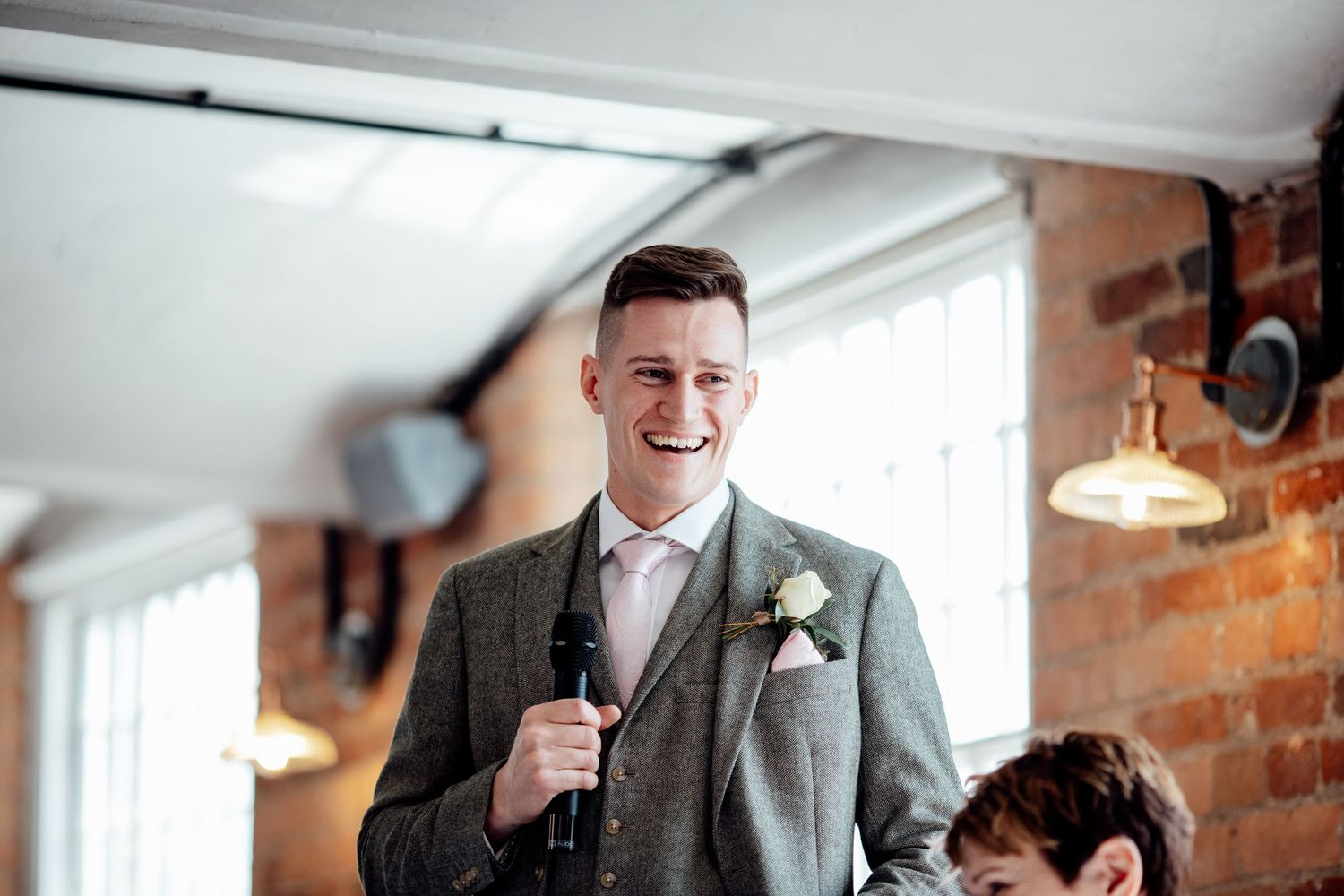 Wedding party sharing laughs in a bright room with exposed brick walls.