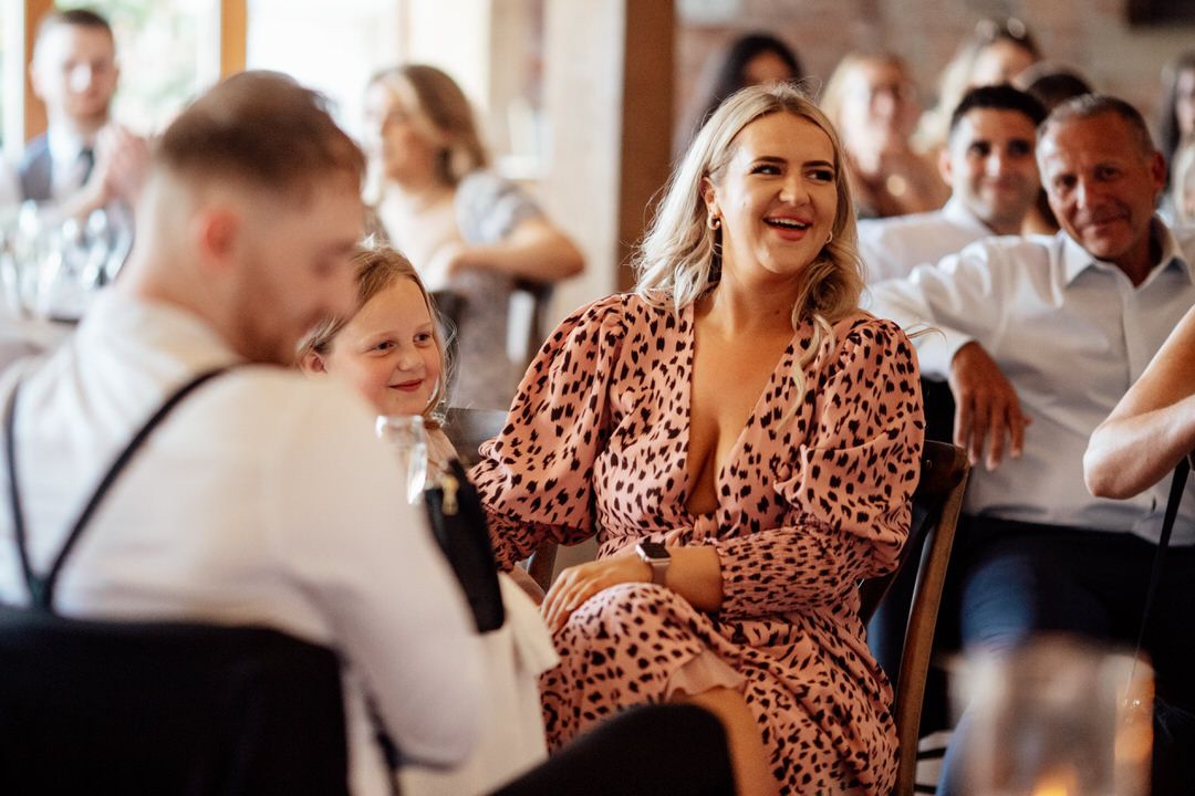 Wedding guests enjoying celebration in rustic indoor venue with natural lighting.