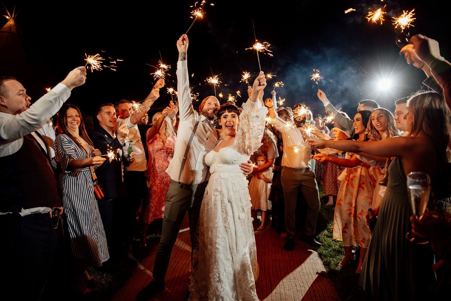 Wedding guests holding sparklers during nighttime celebration creating magical light trails.