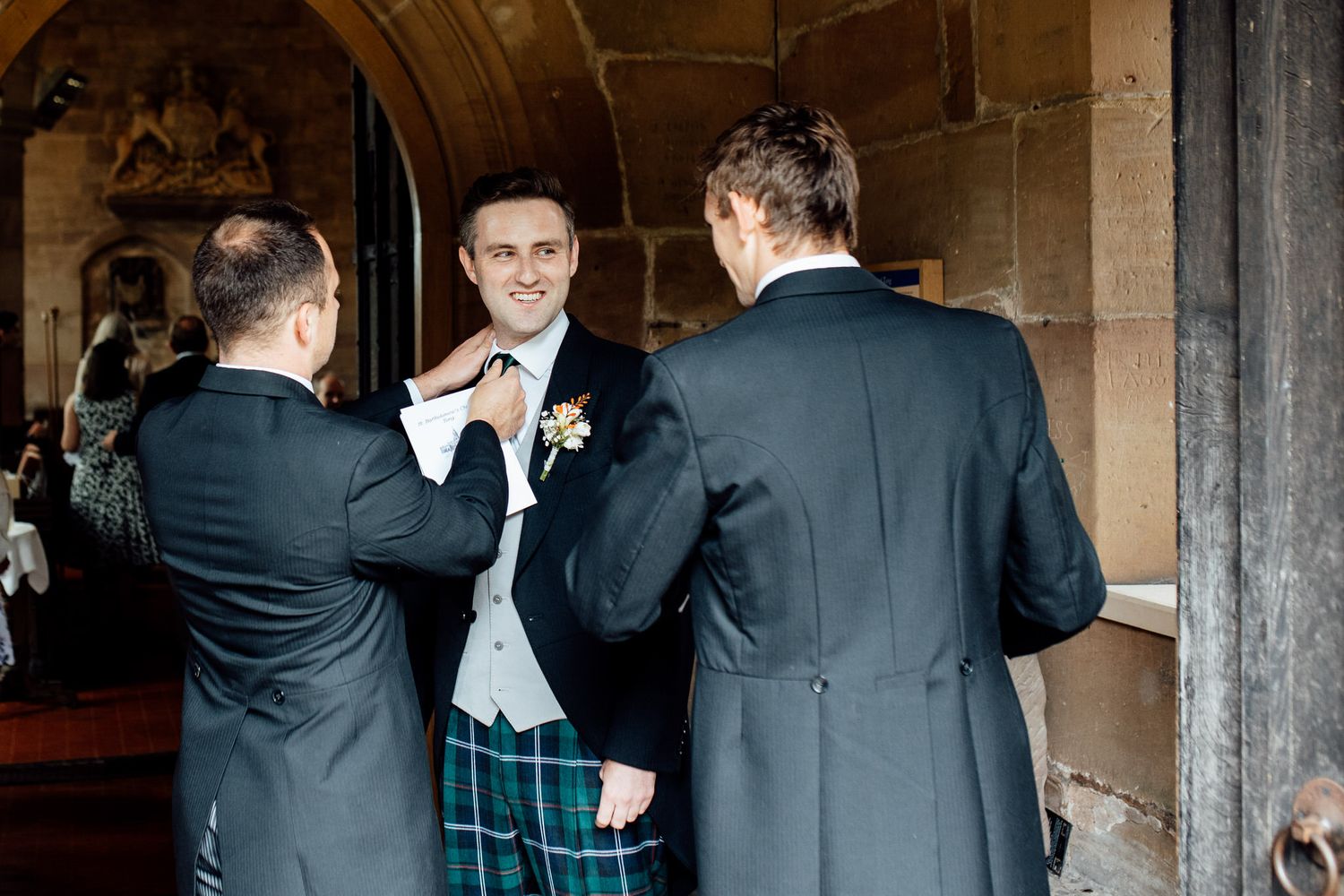 Groomsmen in formal attire gathered in a stone archway.
