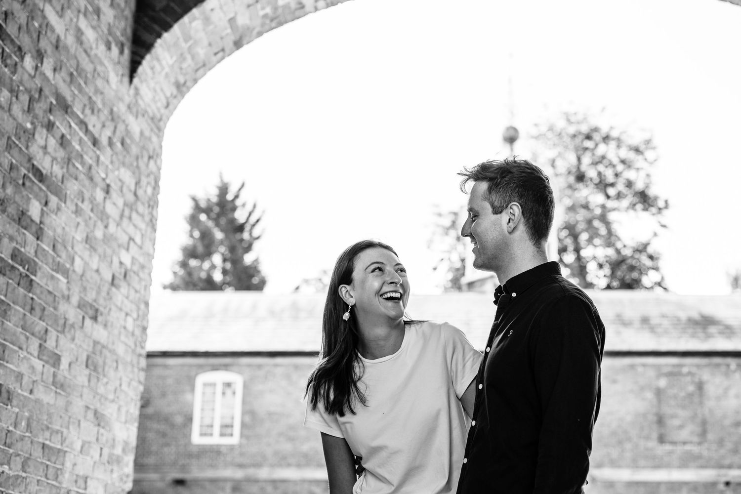 Couple laughing together against white wall in casual portrait session.
