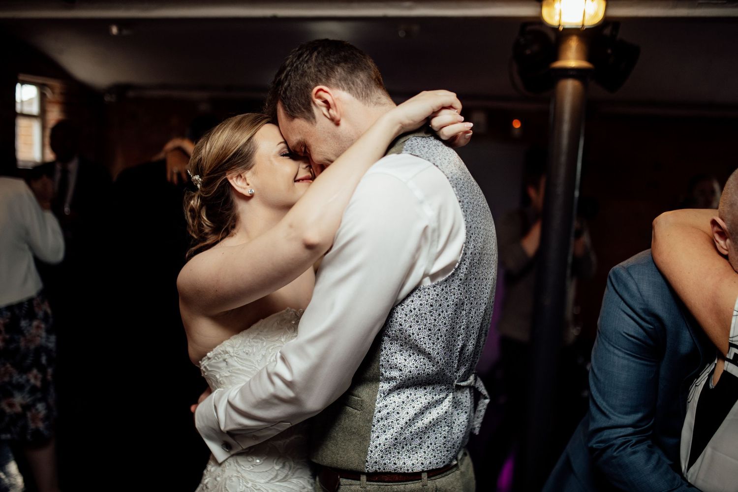 Wedding guests dancing and celebrating in a rustic indoor venue with ambient lighting.