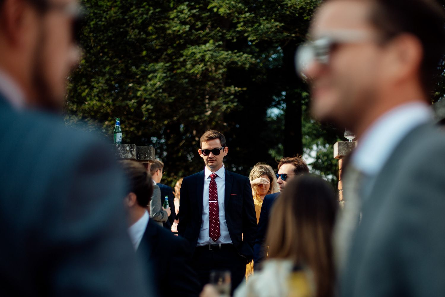 Wedding guests in formal attire gathered outdoors on a sunny day.