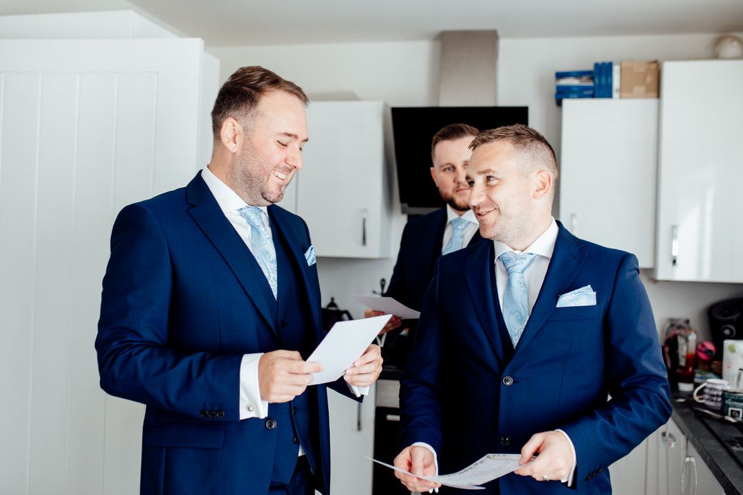 Groomsmen in navy suits and white shirts gather in bright modern room.
