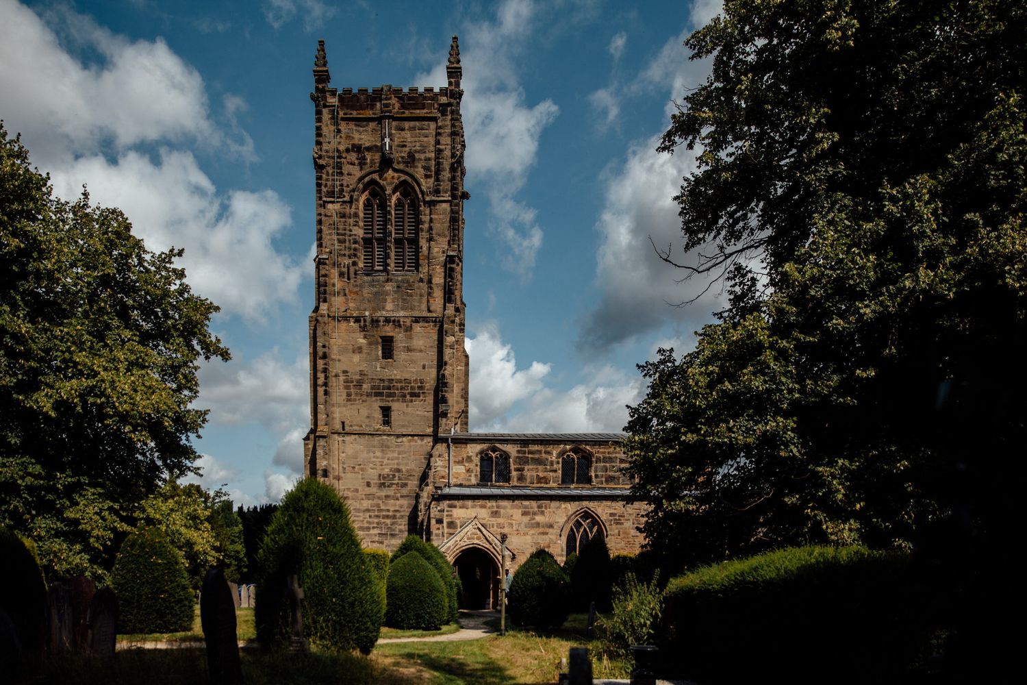 Historic stone church with tall spire against blue summer sky.