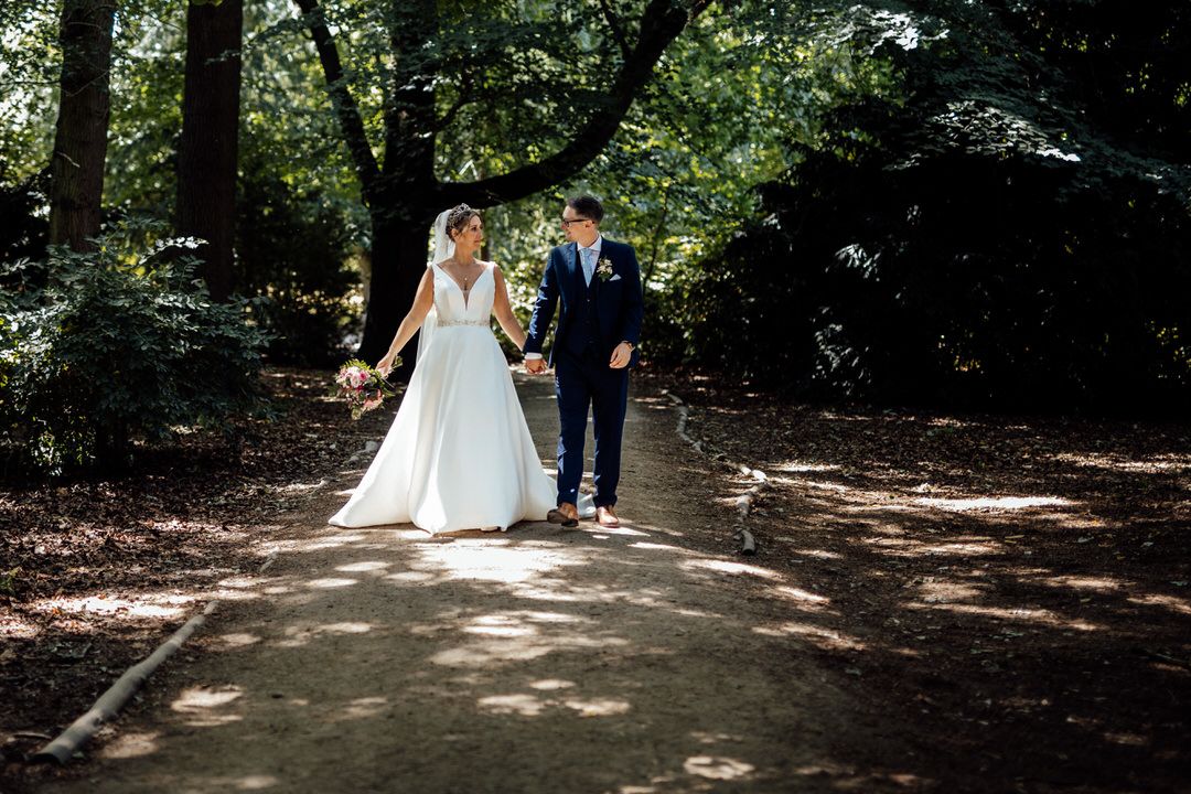 Wedding couple walking through a tree-lined garden path.