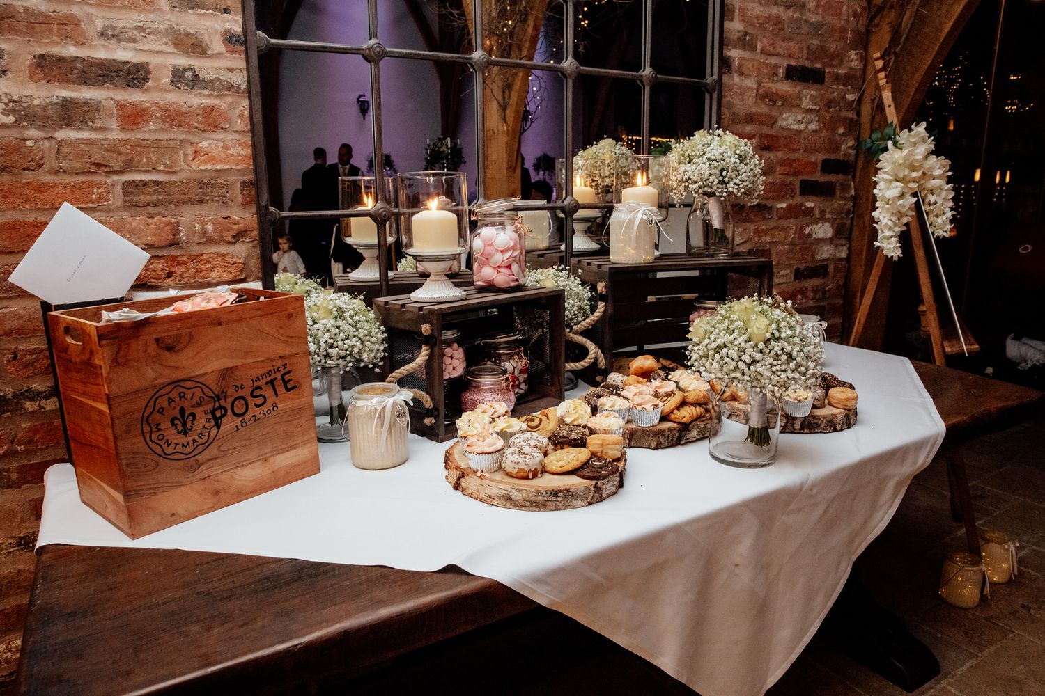 Rustic dessert table with white flowers and treats displayed against exposed brick wall.