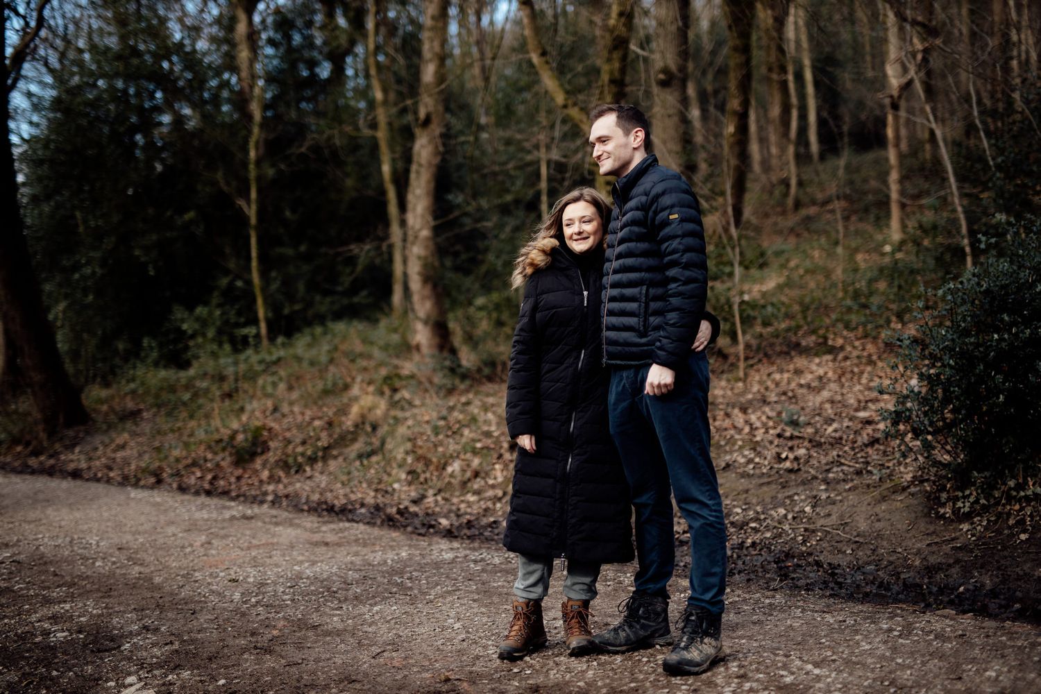 Two people share an intimate moment while walking along a forest path in winter.