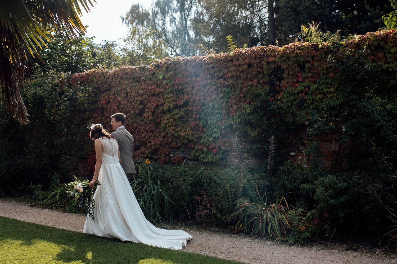 A wedding couple walking through a lush garden pathway surrounded by greenery.