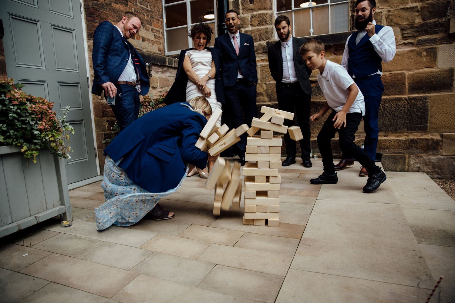 Wedding party playing giant Jenga game on stone patio.