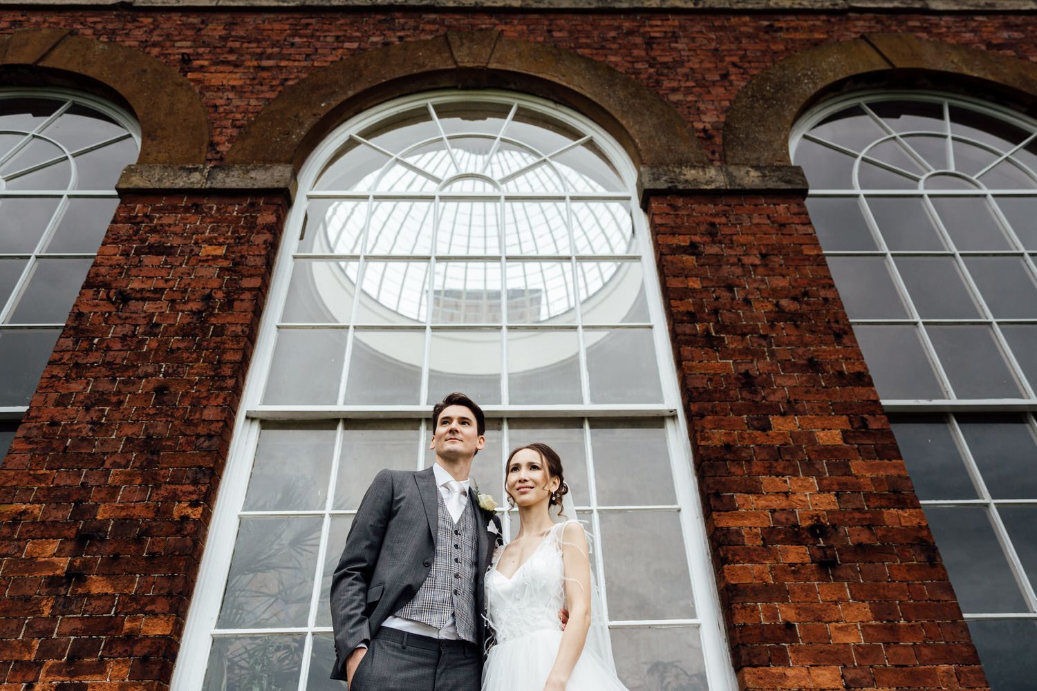 Wedding couple poses in front of historic brick building with arched windows.